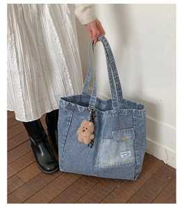 Close-up of blue striped denim tote bag with a brown plush bear charm and front flap pocket