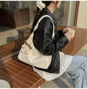 Detail of white leather tote bag with unique knot strap and plush bear charm in outdoor setting