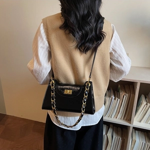Sac à bandoulière élégant en cuir verni noir avec chaîne dorée sur un mannequin