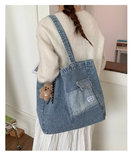 Detail of blue striped denim tote bag with plush bear charm worn on shoulder
