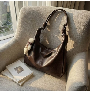 Detail of hobo bag with knotted leather strap, shiny dark brown leather and bear charm