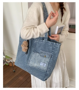 Detailed side view of blue striped denim tote bag worn with bear charm and chic outfit