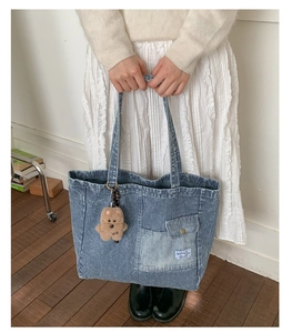 Detail of blue striped canvas tote bag featuring front flap pocket and plush bear charm