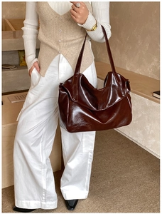 Detail of deep brown glossy leather tote bag with wide shoulder strap and metal rivets