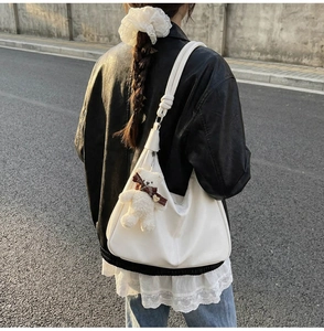 Outdoor shot of white leather tote bag with teddy bear charm shown on model shoulder