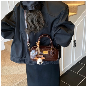Detail of dark brown glossy leather Boston bag featuring a plush dog charm and gold hardware