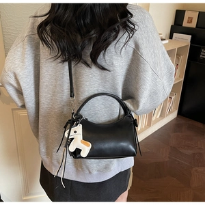 Detalle de un bolso negro con colgante de caballo y correa ajustable usado por modelo