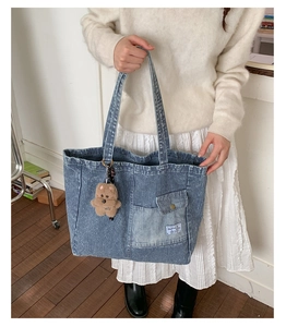 Detail of striped denim tote bag featuring a cute plush bear charm and pocket label