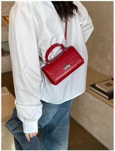 Detail showing red crocodile pattern handbag worn crossbody on model for size perspective