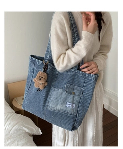 Detail of blue striped canvas tote bag with outer pocket and brown teddy bear charm