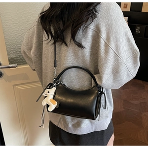 Vista de modelo de bolso media luna negro en cuero con correa y colgante de dibujo animado