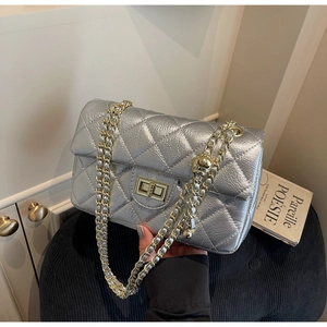 Detailed macro view of metallic silver quilted bag with gold ball chain and twist lock