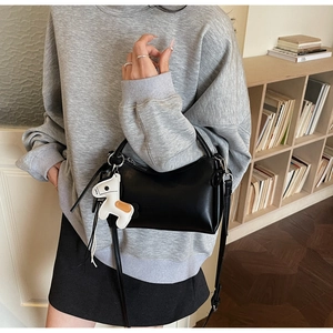 Detalle del bolso de mano negro con un colgante de caballo blanco y correa doble