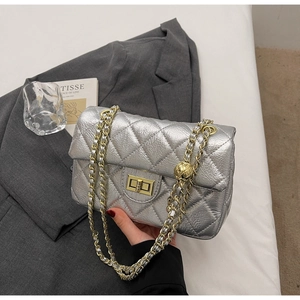 Macro detail of silver quilted leather texture with gold metal chain and sphere buckle