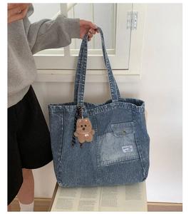 Detail of blue denim tote bag with vertical stripes, front pocket and plush bear charm