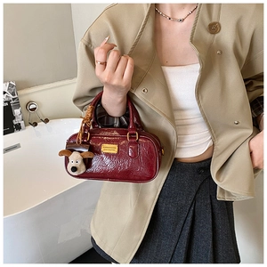 Detail of burgundy glossy leather bowling bag featuring a plush dog charm and gold plaque