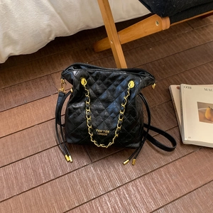 Élégant sac seau en cuir matelassé noir avec chaîne dorée sur un sol en bois chaud