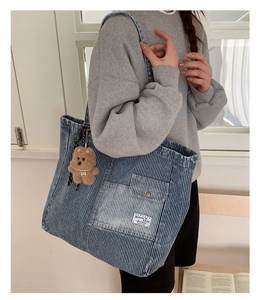 Detail of striped denim tote bag showing the front pocket and plush bear pendant
