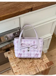 Detail of purple plaid handbag with bow, heart pendant and cat prints on a woven stool
