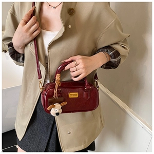 Detail of burgundy glossy pleated shoulder bag with gold metal plate and dog charm