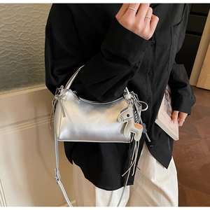 Detalle de bolso de cuero plateado metalizado con colgante de caballo y bandolera fina