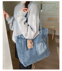 Detail of blue striped denim tote bag with exterior pocket and brown plush bear charm