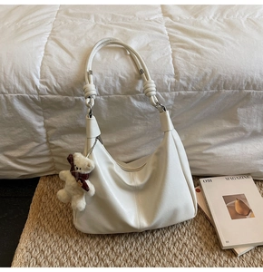 Detail of matte cream tote bag featuring a knotted strap and a small teddy bear charm