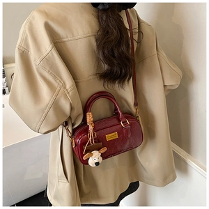 Detail view of burgundy patent leather bag with gold logo and plush puppy pendant