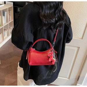 Detalle de bolso rojo en cuero mate con colgante de poni y correa tejida en modelo