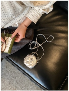 Détail d'un mini sac rond argenté matelassé avec fleur en métal et bandoulière chaîne