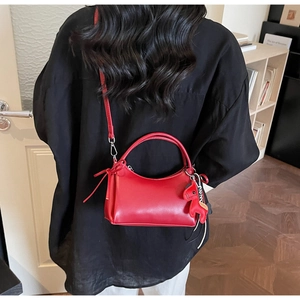 Detalle de bolso de cuero rojo semicircular con adorno de poni y correa larga
