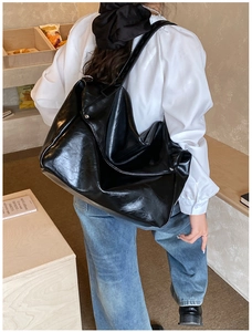 Detail shot of black glossy oil wax leather tote bag showing soft texture and metal buckle