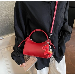 Detalle de bolso de cuero rojo con colgante de caballo y correa de hombro ajustable mujer