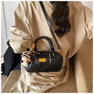 Detail of black bowling bag with wrinkled texture, gold hardware and plush dog charm