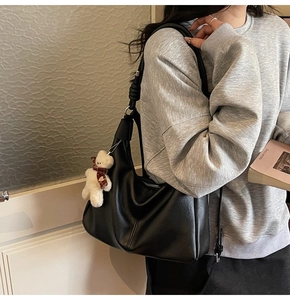 Detail of black faux leather hobo bag with knotted strap and white bear plush charm