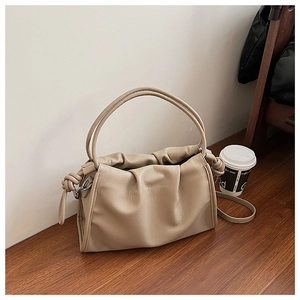 Close-up of light brown pleated leather bag with knot detail on a wooden surface