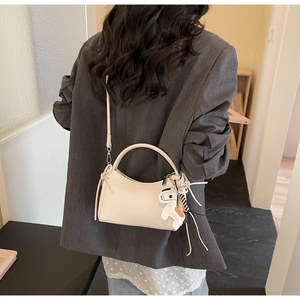 Detalle de un bolso beige en forma de media luna con colgante de caballo y borla