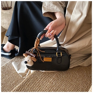 Detail of black patent bowling bag featuring a plush puppy charm and golden metal hardware