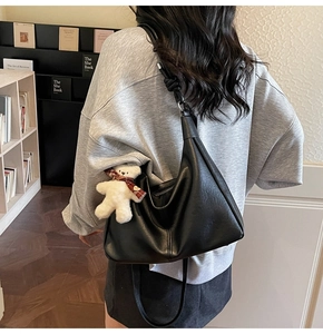 Detail of black leather hobo bag featuring knotted shoulder strap and white bear charm