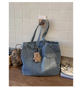 Detail view of blue striped denim tote bag with brown plush bear charm on wooden desk