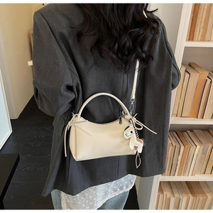 Detalle de bolso blanco crema con colgante de caballo sobre un blazer gris