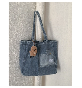 Detail of striped denim tote bag with front pocket and a cute brown plush bear charm