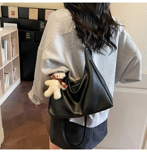 Detail of a black leather hobo bag with a cute white teddy bear plush charm on the strap