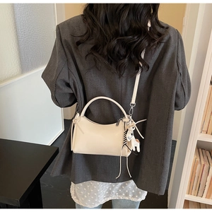 Detalle del bolso crema con correa de rayas y colgante de caballo sobre un traje gris