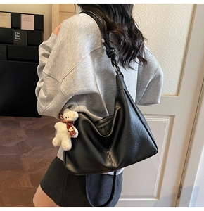 Detail of a large black leather hobo bag with a cute white teddy bear bag charm