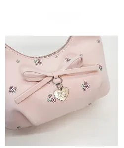 Détail du sac demi-lune rose avec imprimé fleuri, nœud en cuir et pendentif doré