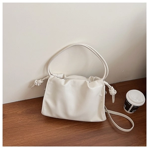 Close-up of cream white lychee texture leather bag with knotted side detail on wood