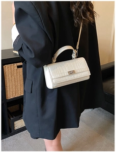 Detailed view of white crocodile pattern handbag with silver twist lock on black blazer