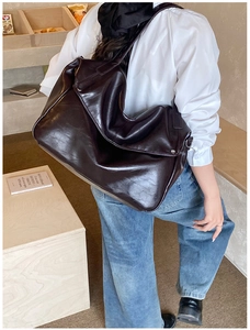Detail of a large glossy deep brown faux leather tote bag worn by a model in a casual setting