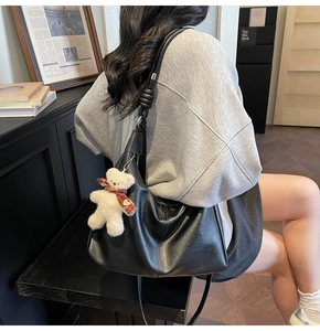 Detail of black faux leather hobo bag featuring a unique knotted shoulder strap and plush bear charm